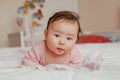 Cute adorable Asian mixed race smiling baby girl four months old lying on tummy on bed Royalty Free Stock Photo