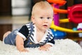 Portrait of cute adorable blond Caucasian smiling baby boy with blue eyes lying on floor in kids children room Royalty Free Stock Photo