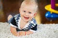 Portrait of cute adorable blond Caucasian smiling baby boy with blue eyes lying on floor in kids children room Royalty Free Stock Photo