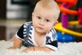 Portrait of cute adorable blond Caucasian smiling baby boy with blue eyes lying on floor in kids children room Royalty Free Stock Photo