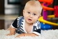 Portrait of cute adorable blond Caucasian smiling baby boy with blue eyes lying on floor in kids children room Royalty Free Stock Photo
