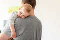 Portrait of cute adorable blond caucasian toddler boy sleeping on fathers shoulder indoors. Sweet little child feeling safety and