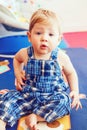 Portrait of cute adorable blonde Caucasian smiling baby boy with brown eyes in blue romper sitting on floor in kids room Royalty Free Stock Photo