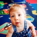 Portrait of cute adorable blonde Caucasian smiling baby boy with brown eyes in blue romper sitting on floor in kids room Royalty Free Stock Photo