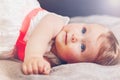 Portrait of cute adorable blonde Caucasian smiling baby child girl with blue eyes in white dress with red bow lying on bed Royalty Free Stock Photo