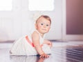 Portrait of cute adorable blonde Caucasian smiling baby child girl with blue eyes in white dress with red bow sitting on floor Royalty Free Stock Photo