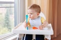 Caucasian child boy with dirty messy face sitting in high chair eating apple puree with spoon Royalty Free Stock Photo