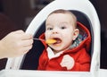 Portrait of cute adorable Caucasian little baby boy sitting in high chair in kitchen eating meal puree Royalty Free Stock Photo