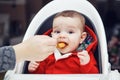 Portrait of cute adorable Caucasian little baby boy sitting in high chair in kitchen eating meal puree Royalty Free Stock Photo