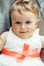 Portrait of cute adorable Caucasian smiling laughing baby girl with blue eyes in white dress with red bow lying on bed looking in Royalty Free Stock Photo