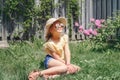 Portrait of cute adorable child girl in sunglasses and a straw hat sitting on grass outdoor. Happy smiling Caucasian kid having Royalty Free Stock Photo