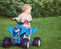 Portrait of cute adorable happy little blond Caucasian boy girl child driving blue electric car in park