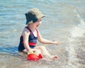 Portrait of cute adorable happy smiling toddler Caucasian girl with hat and watering pot toy on beach sitting in water Royalty Free Stock Photo