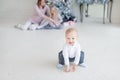 Portrait of cute adorable little blond toddler boy squatting in cozy living room and mother with daughter sitting near christmas Royalty Free Stock Photo