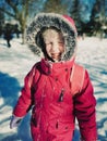 Adorable preschool Caucasian smiling girl squinting her eyes from bright sun on sunny winter day with snow on her face