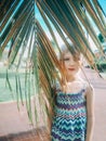 Portrait of cute adorable sad lonely preschool Caucasian little girl child hiding among large old green palm tree leaves Royalty Free Stock Photo