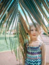 Portrait of cute adorable sad lonely preschool Caucasian little girl child hiding among large old green palm tree leaves Royalty Free Stock Photo