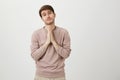 Portrait of cute adult man with bristly holding hands on chest in pray gesture, begging for something with adorable look