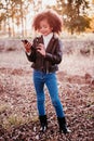 portrait of cute afro kid girl using mobile phone at sunset during golden hour, autumn season, beautiful trees background Royalty Free Stock Photo