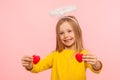 Portrait of cute angelic happy little girl with halo over head holding toy hearts and looking at camera with toothy smile Royalty Free Stock Photo