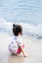 Portrait of cute Asian child girl sitting on the sand beach. Children looks out to the sea. On the beach and waves. Royalty Free Stock Photo