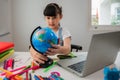 Portrait of cute Asian Child girl student using laptop computer online to learn with a model globe for search the map and country