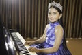 A portrait of a cute Asian girl, makeup, wearing a blue evening dress and a crown, playing the piano Royalty Free Stock Photo