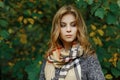 Portrait of a cute attractive young woman in stylish autumn clothes in a park near the yellow-green leaves.