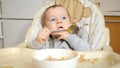 Portrait of cute baby boy with blue eyes eating food with hands and spoon and getting messy Royalty Free Stock Photo