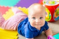Portrait of cute baby boy lying on floor covered with multicolored soft mats in playroom. Adorable toddler kid smiling and playing Royalty Free Stock Photo