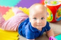 Portrait of cute baby boy lying on floor covered with multicolored soft mats in playroom. Adorable toddler kid smiling and playing