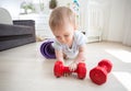 Portrait of cute baby boy palying with red dumbbells on floor at home Royalty Free Stock Photo