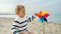 Portrait of cute baby boy sitting on the sandy sea beach and playing with colorful pinwheel. Concept of child happiness during Royalty Free Stock Photo