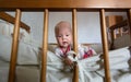 Portrait of cute baby girl with blue eyes is sitting in crib. Adorable infant sits alone in cot and is interested Royalty Free Stock Photo