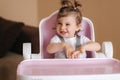 Portrait of cute baby girl sitting in high chair in the kitchen. Adorable little girl waiting for dinner Royalty Free Stock Photo