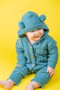 Portrait of a cute baby in a warm knitted jumpsuit with a hood on a yellow background Royalty Free Stock Photo