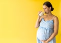 portrait cute beautiful pregnant young pretty woman in floral blue dress holds drink glass of milk rubs tummy on yellow