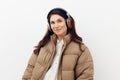 portrait of a cute beautiful woman with long hair standing in brown headphones in a beige stylish down jacket on a light Royalty Free Stock Photo