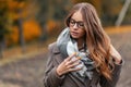 Portrait of a cute beautiful young woman in fashionable glasses with brown long hair in a knitted scarf in a stylish coat. Royalty Free Stock Photo