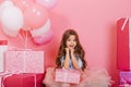 Portrait cute birthday kid expressing to camera suround big giftboxes, balloons on pink background. Amazing