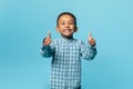 Portrait of cute black boy showing thumbs up and smiling at camera while posing over blue background, studio shot Royalty Free Stock Photo