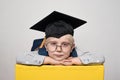 Portrait of a cute blond boy in big glasses, academic hat and a backpack. White background