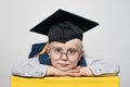 Portrait of a cute blond boy in big glasses, academic hat and a backpack. White background