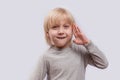 Portrait of cute blond boy on white background. Child holds hand of face and grins Royalty Free Stock Photo