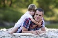 Portrait of cute blond girl hugging young father on pebbled rive Royalty Free Stock Photo