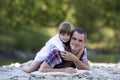 Portrait of cute blond girl hugging young father on pebbled rive Royalty Free Stock Photo