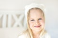 Portrait cute blond girl. Smilling kid in white hat. Child on bed in bright room. Adorable baby wearing funny hat wit Royalty Free Stock Photo