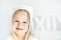 Portrait cute blond preschooler girl. Smilling kid in white hat. Child on bed in nursery room. Adorable baby wearing funny hat Royalty Free Stock Photo