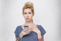 Portrait of cute blonde girl with tattoos hanging cell phone and become confused because her boyfriend has bad news. Royalty Free Stock Photo