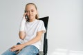 Portrait of sad blonde little girl with broken arm wrapped in plaster bandage talking smartphone, smiling looking down Royalty Free Stock Photo